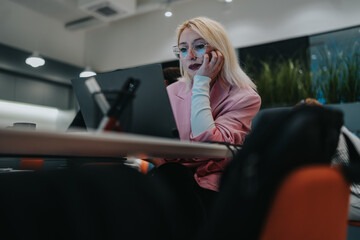 A focused professional woman sits at a modern office desk, talking on a mobile phone while working...