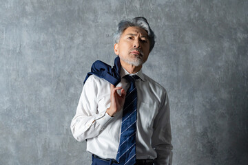 グレー背景の前でジャケットを肩にかけたポーズの男性