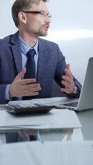 Businessman wearing blue suit is thinking while working with laptop, calculator and documents at...