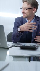 Businessman wearing blue suit is thinking while working with laptop, calculator and documents at...