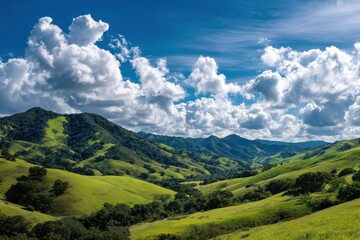 Naklejka premium Serene landscape with lush green hills and verdant mountains under a clear sky filled with fluffy clouds, evoking tranquility and the splendor of nature's untouched beauty