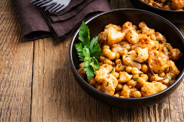 Cauliflower and chickpeas curry salad on wooden table, healthy vegan food
