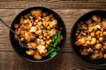 Cauliflower and chickpeas curry salad on wooden table, healthy vegan food