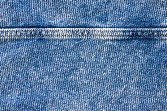Close-up view of blue denim fabric showing detailed stitching and worn texture.