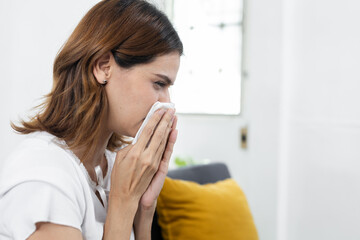 Sick women blowing her nose into a tissue, showing symptoms of cold, flu, allergy, or respiratory infection. Ideal for use in health, medical, seasonal illness or virus related content.