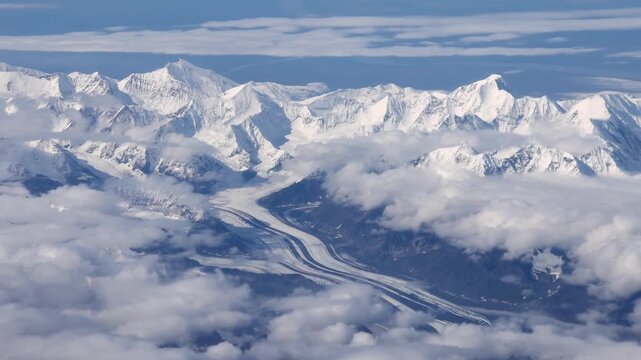 Aerial view of majestic snow-capped mountain peaks piercing through a sea of fluffy white clouds and a glacier, Denali, Alaska, United States.