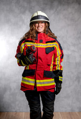 Feuerwehrfrau in Schutzkleidung und Helm, mit Hohlstrahlrohr, Studioaufnahme vor Betonwand.