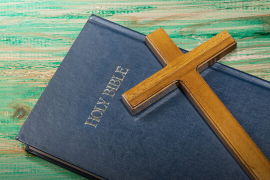 Blue book of the Holy bible and a Christian cross on a wooden table. Symbol of faith in God. Concept of Spirituality, Christianity, religion, faith, Jesus, or belief