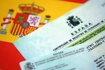 Citizenship or naturalization certificate document and card on flag of Spain close up
