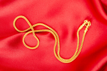 Fototapeta premium Gold chain necklace on red silk textile.