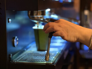 Barista preparing milk in a coffee machine for adding to coffee. Female hands are making coffee using professional metal machine in cafe. Barista is heating milk, whipping foam with frother, steam. 