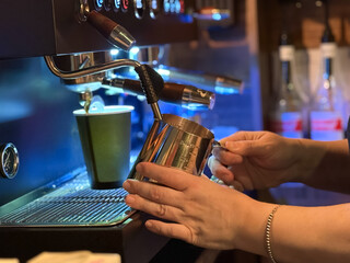 Barista preparing milk in a coffee machine for adding to coffee. Female hands are making coffee using professional metal machine in cafe. Barista is heating milk, whipping foam with frother, steam. 