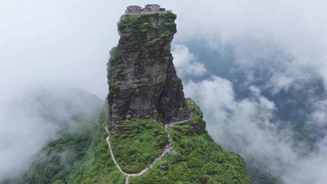 Aerial view of the Fanjingshan peak rising majestically above the clouds, with winding paths and temples, enveloped in mist, Fanjingshan, Guizhou, China.