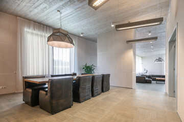 A modern dining area with a large wooden table surrounded by black leather armchairs and natural lighting in a modern interior.