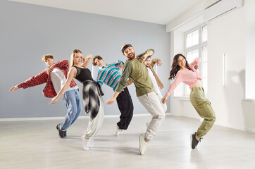Happy young sporty people group dancing together having dance sport workout in modern studio. Men and women learning movements during a class. Active lifestyle and training concept.