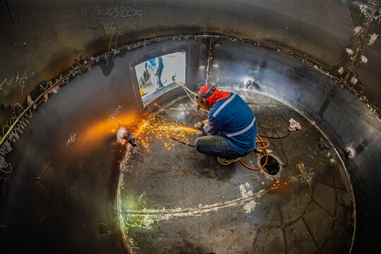 Welding male worker metal is part of machinery bottom plate tank construction flash spark inside confined