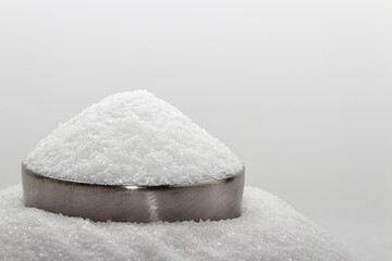 Iodated salt pile is poured into metal container in front of white background, with wooden spoon. Sitting on another pile of salt. Textured horizontal photo, closeup. V20
