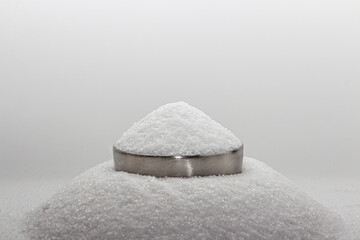 Iodated salt pile is poured into metal container in front of white background, with wooden spoon. Sitting on another pile of salt. Textured horizontal photo, closeup. V24