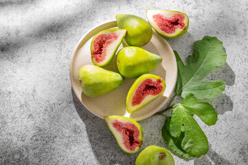 Sweet green figs in a plate a on a gray concrete background with leaves and sunlight.