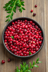 layout of fresh cranberries in a dark bowl on a wooden background with green branch.