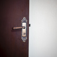 Close de uma porta de madeira antiga entreaberta com maçaneta metálica decorativa, representando transição, mistério e o conceito de passagem