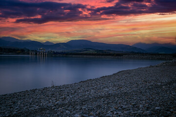 Reservoir water reflecting vibrant sky and distant mountains with a concrete structure