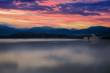 Vibrant sunset sky over mountains reflecting on the tranquil surface of a reservoir