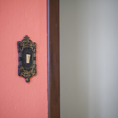Close artístico de interruptor antigo, com moldura ornamentada em parede vermelha, sugerindo nostalgia, design clássico e contraste entre tradição e modernidade