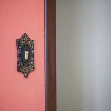 Close art&iacute;stico de interruptor antigo, com moldura ornamentada em parede vermelha, sugerindo nostalgia, design cl&aacute;ssico e contraste entre tradi&ccedil;&atilde;o e modernidade