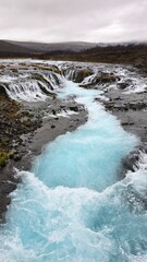 The vivid glacial-blue stream of Brúarfoss Waterfall flows through rugged lava rocks and moss, creating one of Iceland’s most photogenic and unique natural scenes.