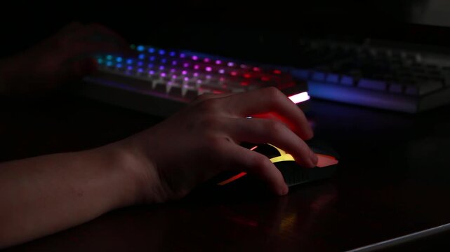 Gaming setup with hand on mouse and illuminated keyboard in dark room