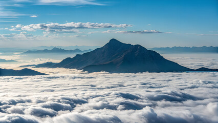 Mountain peak rising above a sea of clouds under a blue sky , Peaceful sky and distant mountain view from above the clouds.
