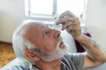 Man putting liquid drops in his eye solving vision problem.Senior dropping eye drop medicine...