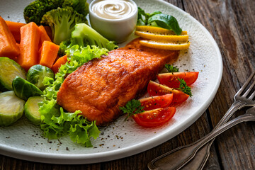 Fried salmon steak with boiled broccoli, brussels sprouts and carrots and mayonnaise on wooden table	