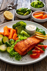 Fried salmon steak with boiled broccoli, brussels sprouts and carrots and mayonnaise on wooden table	