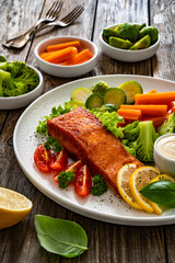 Fried salmon steak with boiled broccoli, brussels sprouts and carrots and mayonnaise on wooden table	
