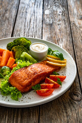 Fried salmon steak with boiled broccoli, brussels sprouts and carrots and mayonnaise on wooden table	