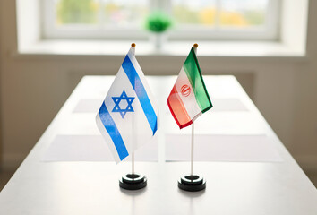 Flags signal diplomacy at a negotiation meeting. On a table, Israel and Iran flags stand, marking...