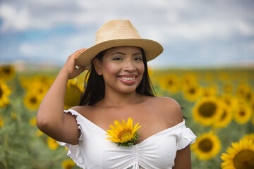 Portrait of a young, dark-skinned Latin woman farmer wearing a white shirt and straw hat standing...