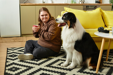 Young woman enjoys a cozy moment at home with her dog and a warm drink