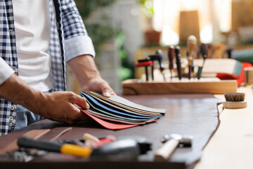 Male artisan organizing colorful leather swatches in workshop with tools