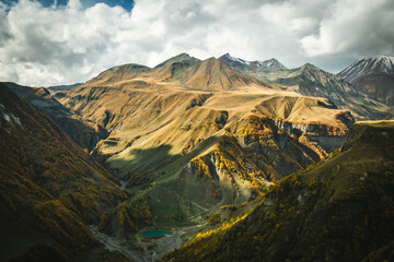 Majestic autumn landscape of the Caucasus mountains in Georgia with golden slopes and a small turquoise lake in the valley. Dramatic light and vibrant colors of untouched nature