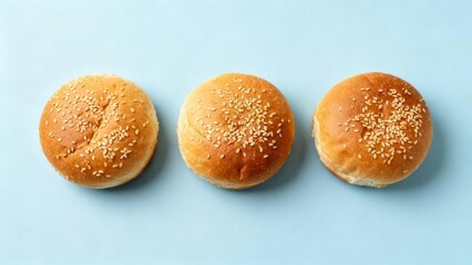 Three golden baked bread rolls topped with sesame seeds are aligned horizontally above a light blue background