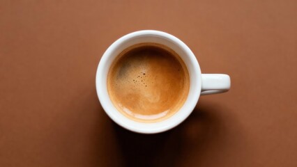Overhead view captures rich brown espresso drink crowned with crema in a white ceramic cup resting on a solid warm brown surface