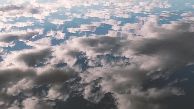Blue sky reflection. Clouds drift on wavy water. Calm natural texture