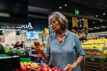 Senior woman choosing fresh fruit at grocery store
