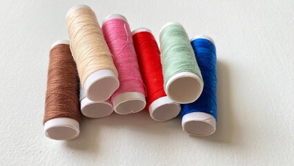 Several rolls of sewing thread in various colors are arranged irregularly on a white background.