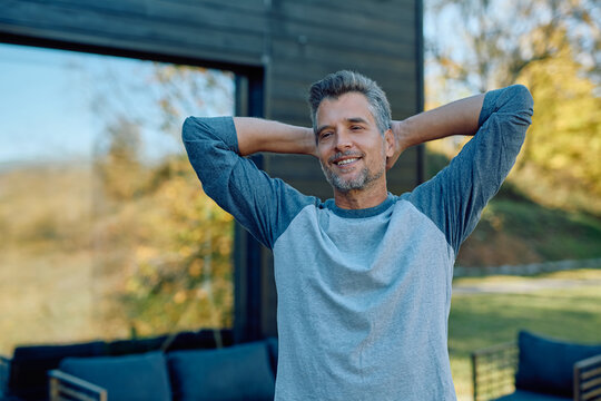 Happy man standing with hands behind head, enjoying a peaceful moment outside his contemporary house