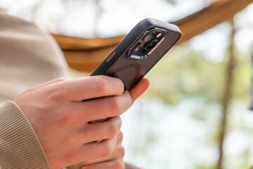 Person scrolling smartphone in hammock area outdoors on sunny day