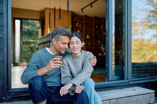 Couple sitting on a porch, embracing and sharing a tender moment with coffee. Relaxing together in a cozy outdoor setting